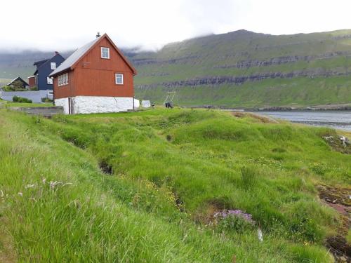 a red barn on a grassy hill next to a body of water at The Old Store in Hellur