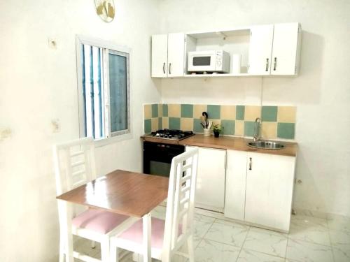 a kitchen with white cabinets and a table and a microwave at Gêna house in Douala