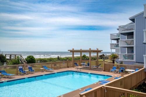 Una piscina con sillas y el océano al fondo. en Oceanfront Condo with pool - Walk to the Tiki Bar, en Carolina Beach
