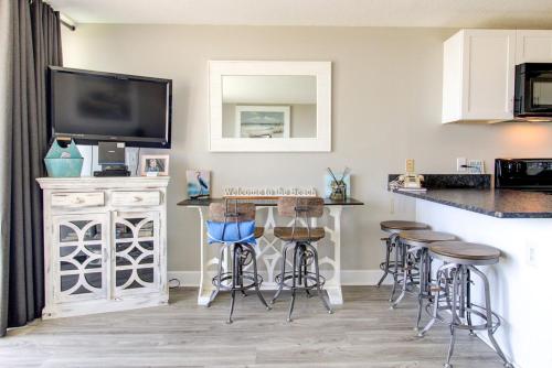 a kitchen with a bar with stools and a tv at 0103 Relax You're At The Beach by Atlantic Towers in Carolina Beach