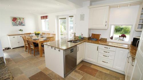 a kitchen with white cabinets and a dining room with a table at Trelau in Parkmill