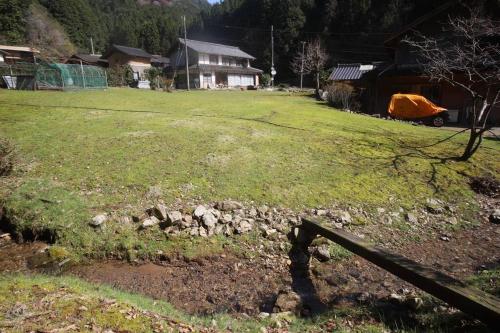 a field of grass with a fence and a house at 里山アウトドアフィールド・古民家コテージとろせ in Gujo