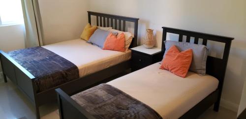 2 camas en una habitación pequeña con almohadas de color naranja y azul en Ubuntu De La Villa- Palm View Estate en Mammee Bay