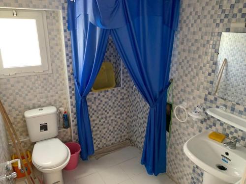 a bathroom with a toilet and a sink with blue curtains at Pleasant house in Africa Jade 200m to the beach in Korba