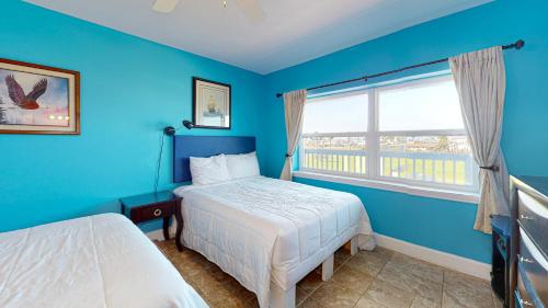 a blue bedroom with a bed and a window at SIV10 Beautiful Condo, Shared Pool, Close to Beach in Port Aransas