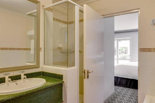 a bathroom with a sink and a shower and a bed at Protea Hotel by Marriott Cape Town Mowbray in Cape Town