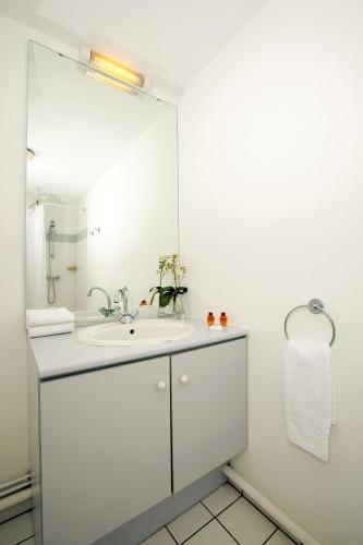 une salle de bain blanche avec un lavabo et un miroir dans l'établissement Séjours & Affaires Nantes Ducs De Bretagne, à Nantes