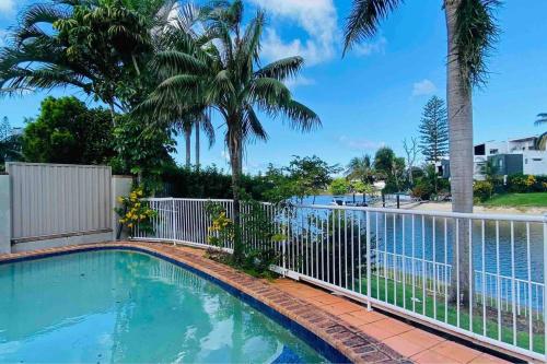 a swimming pool with a fence and palm trees at Charming 4 Bedroom Waterfront Home W/ Pool Near Casino in Gold Coast