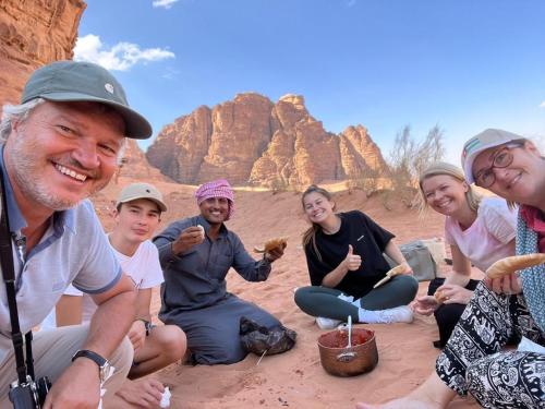 a group of people sitting in the desert eating food at WADI RUM-Bedouin Tents and Jeep Tours in Wadi Rum