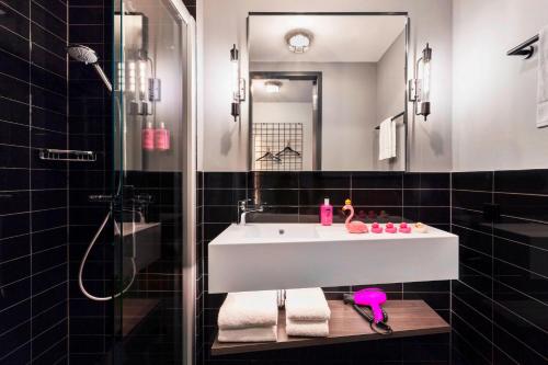La salle de bains est pourvue d'un lavabo blanc et d'une douche. dans l'établissement Moxy Darmstadt, à Darmstadt