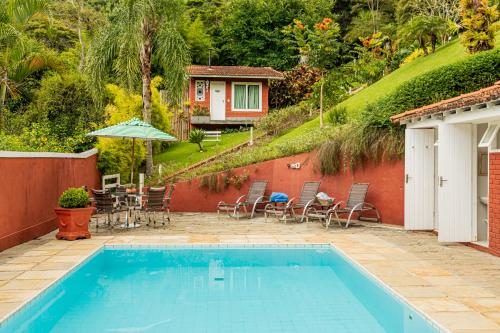 une piscine avec une table et des chaises ainsi qu'une maison dans l'établissement Su Paradise Chalés e Suítes, à Itaipava