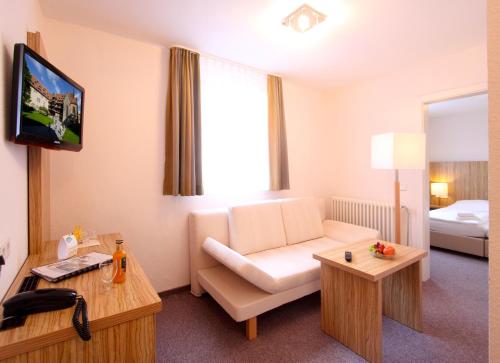 a hotel room with a white couch and a television at Akzent Hotel Am Burgholz in Tabarz
