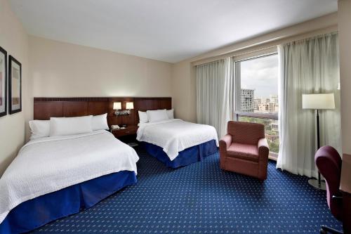 a hotel room with two beds and a chair and a window at Courtyard by Marriott San Juan Miramar in San Juan