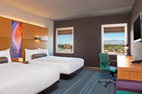 a hotel room with two beds and a desk and two windows at Aloft Tucson University in Tucson