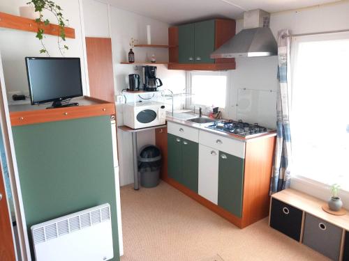 cocina pequeña con armarios verdes y blancos y TV en Bungalow, en Sainte-Marie-du-Mont