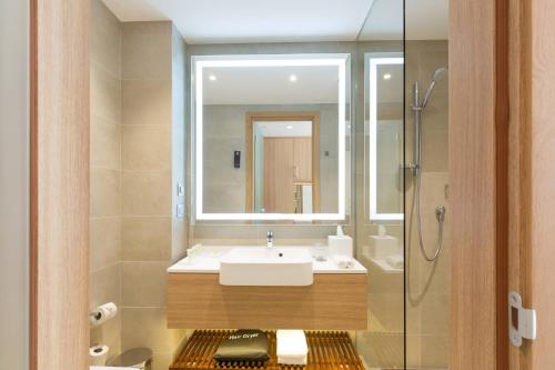 ein Bad mit einem Waschbecken, einem Spiegel und einer Dusche in der Unterkunft Courtyard by Marriott Banja Luka in Banja Luka