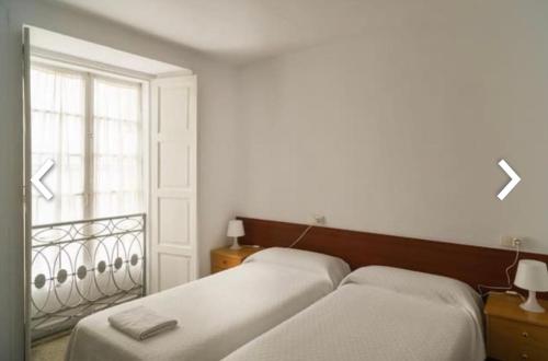 two beds in a room with a window at Casa Anglicana del Peregrino/ Pensión Santa Cristina in Santiago de Compostela