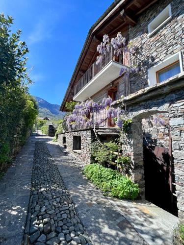 a stone house with a balcony with purple flowers on it at Casa Unica- da Bruno in Colico
