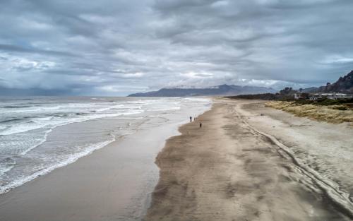 a beach with people walking on the sand at Seabatical on The Strand - Meredith Lodging in Rockaway Beach