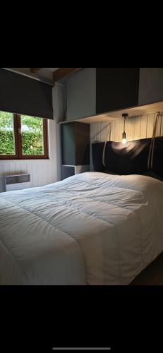 un grand lit blanc dans une chambre avec une fenêtre dans l'établissement Gîte chalet bleu soleil, à Saint-Benoît-dʼHérbertot