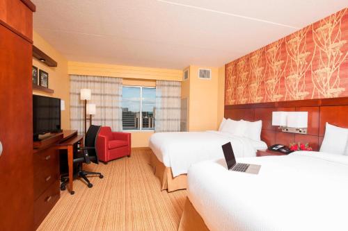 a hotel room with two beds and a desk and a television at Courtyard Peoria Downtown in Peoria