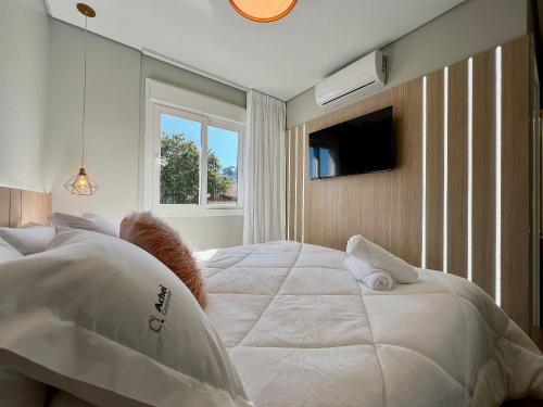 1 dormitorio con 1 cama blanca grande y TV en Apartamento Res Aire 3 Suítes by Achei Gramado, en Gramado