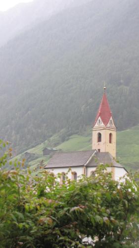 a church with a red roof on top of a hill at Hotel Am Fels in Senales