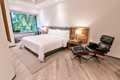 a bedroom with a bed and two chairs and a window at GHL Hotel Portón Medellín in Medellín