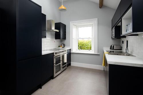 une cuisine avec des armoires noires et une fenêtre dans l'établissement Millers Cottage, à Berwick-upon-Tweed