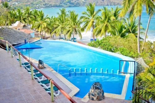 una gran piscina azul con palmeras y el océano en Hotel Catalina Beach Resort, en Zihuatanejo