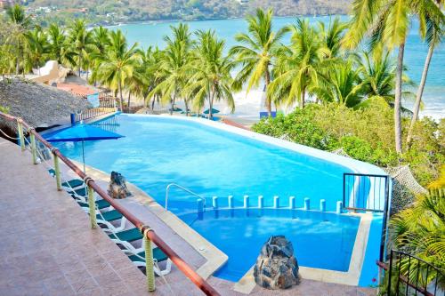 a large blue swimming pool with palm trees and the ocean at Hotel Catalina Beach Resort in Zihuatanejo