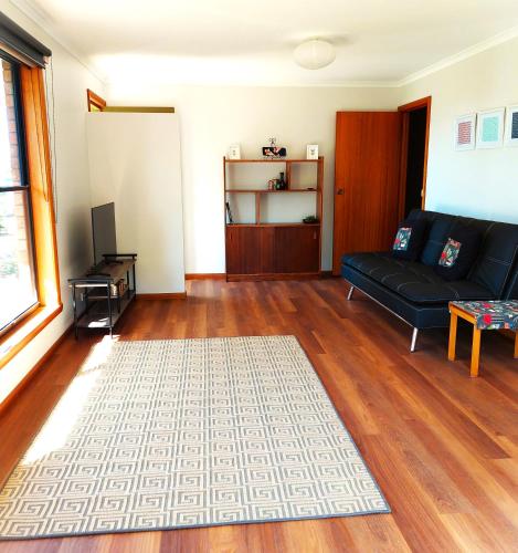 a living room with a black couch and a wooden floor at Percy's Cottage in Devonport