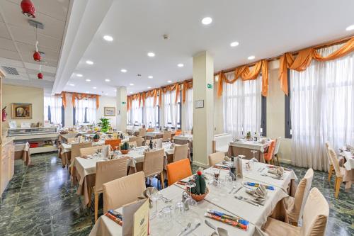 un ristorante con tavoli e sedie bianchi e finestre di Hotel Europa a San Bartolomeo al Mare