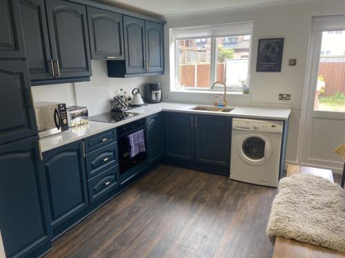 a kitchen with blue cabinets and a washing machine at Lovely 2 Bed Full House By The Beach in Liverpool