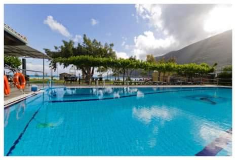 a large blue swimming pool with a mountain in the background at Porto Fico Hotel in Vasiliki