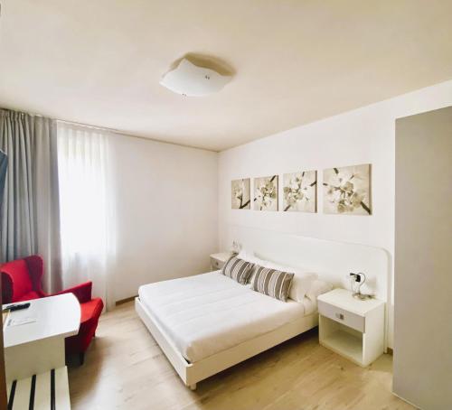 a white bedroom with a bed and a red chair at Alle Porte in Riva del Garda