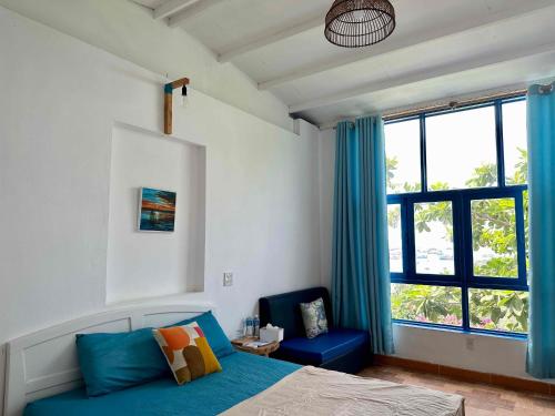 a bedroom with a bed and a blue chair and a window at IRINI Boutique Homestay Mui Ne in Mui Ne