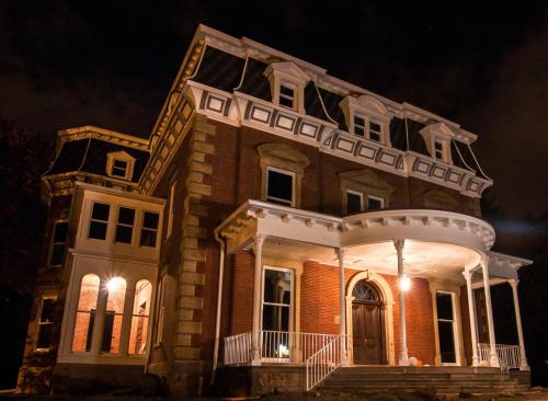 a large brick house with a porch at night at Steele Mansion Inn & Gathering Hub in Painesville