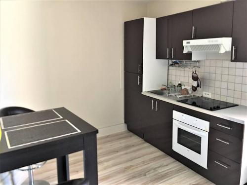 La cuisine est équipée de placards noirs et d'un four avec plaques de cuisson blanches. dans l'établissement Appartement 3 pièces pleins de charmes (Virginie), à Montbéliard