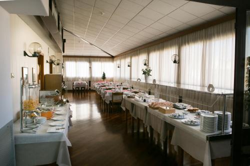 une rangée de tables dans une grande pièce avec des tables blanches dans l'établissement Hotel Giardino, à Follonica