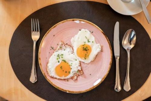 two eggs on a pink plate on a table with silverware at Posthotel Radstadt in Radstadt