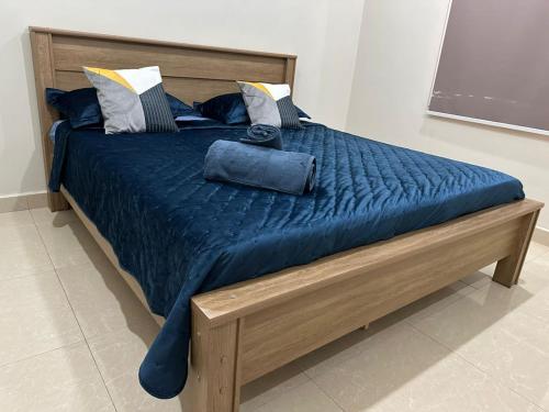 ein Holzbett mit einer blauen Bettdecke und Kissen in der Unterkunft Janneya Apartments in Sukuta