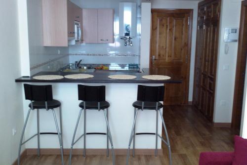 a kitchen with a counter with three bar stools at Apartamentos Reservas León in San Isidro