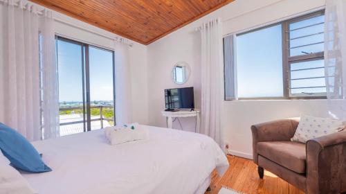 a bedroom with a bed and a chair and windows at Suikerbekkie in Struisbaai