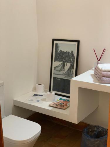 a white bathroom with a toilet and a picture at Baleias home in Praia do Forte