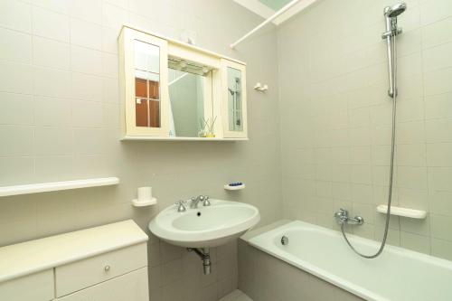 La salle de bains blanche est pourvue d'un lavabo et d'une douche. dans l'établissement Confortevole Bilocale Giardino Doppio Parcheggio, à Punta Ala