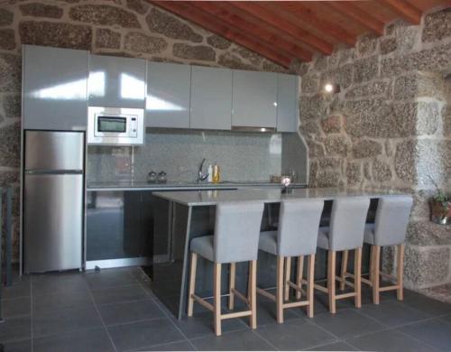 a kitchen with a counter with white cabinets and bar stools at Cantinho da Pereira in Lugar