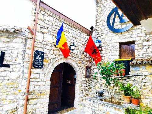 um edifício de pedra com bandeiras na lateral em Guva Mangalem Hotel Restaurant em Berati