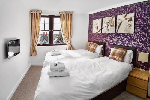 two beds in a bedroom with purple wallpaper at Thistle Apartments - Rose Apartment in Aberdeen