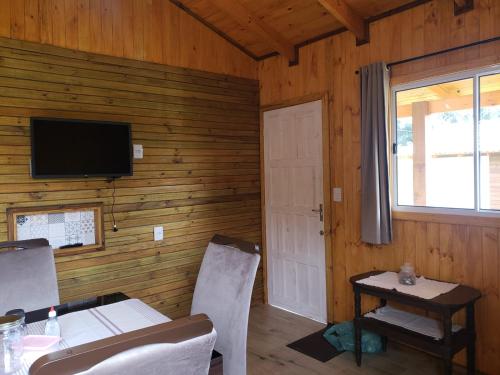 uma sala de jantar com uma mesa e uma televisão numa parede de madeira em Cabana Azinheira em Urubici